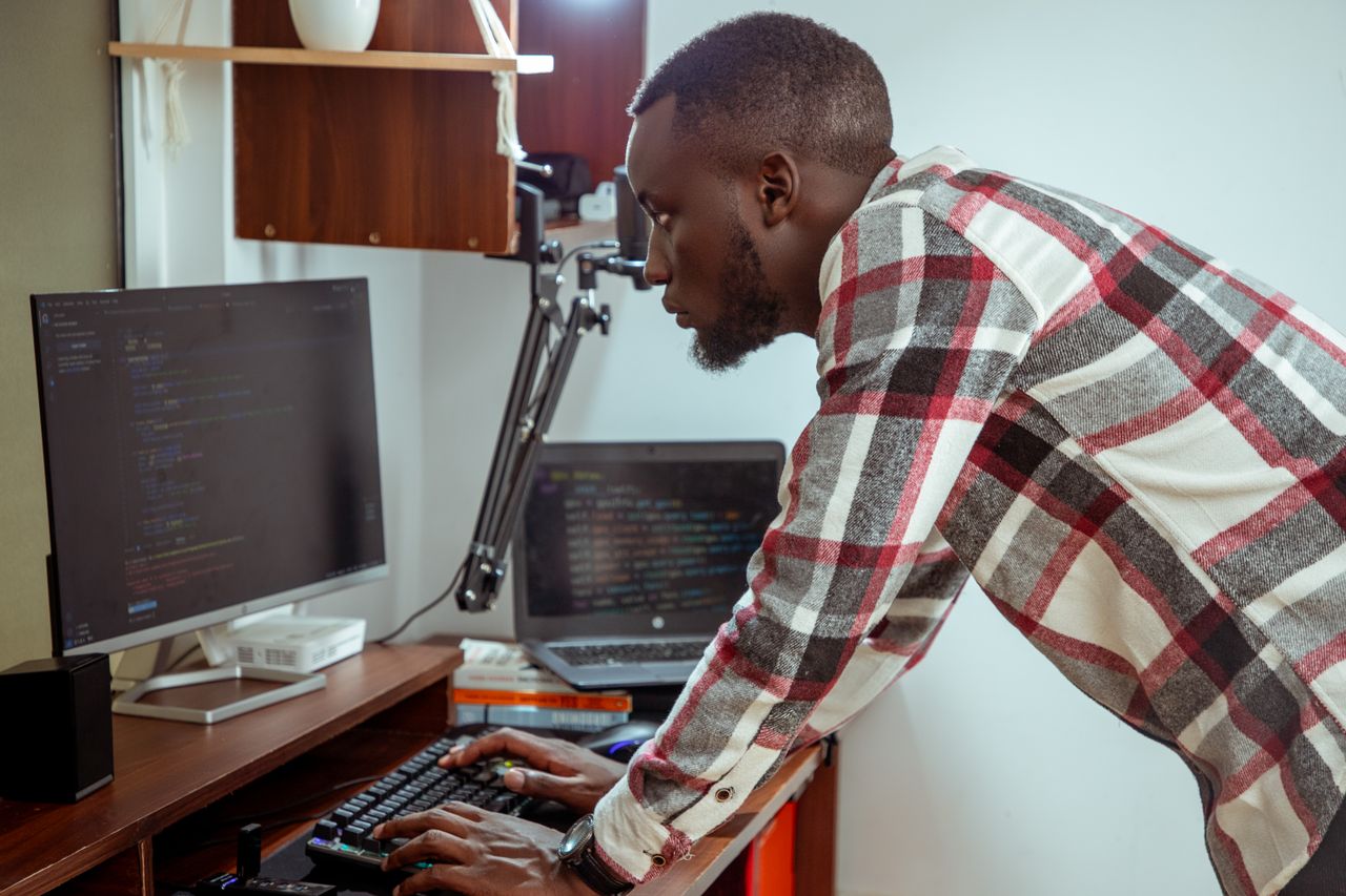 About Focused IT specialist in casual attire working at a computer in a modern office setting.